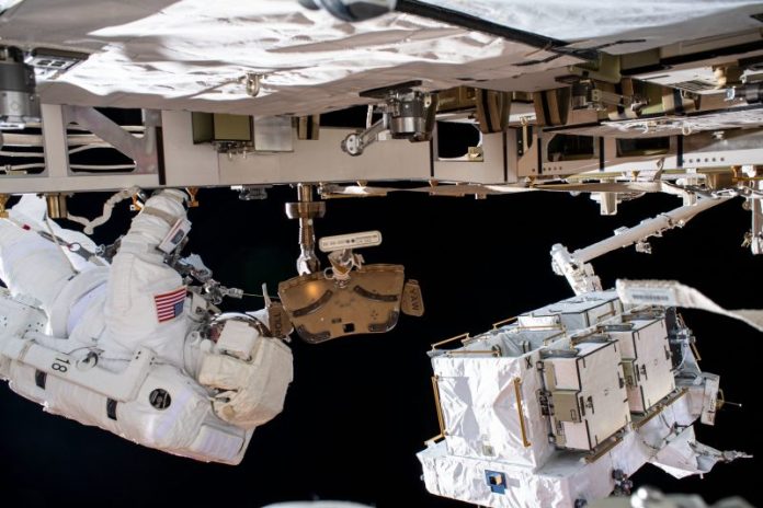 Astronaut in spacesuit outside spacecraft with white-covered box at end of jointed arm.