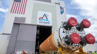 a rocket on its side going into a large building that has banners for the artemis program, the u.s. flag and nasa at the top