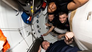 four smiling people aboard a spacecraft