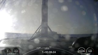 A black and white spacex falcon 9 rocket first stage sits on the deck of a ship at sea.