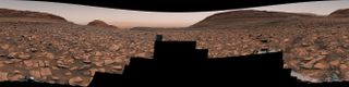 a partial panoramic view of a rusty landscape with large broken rocks embedded in the redbrown ground.