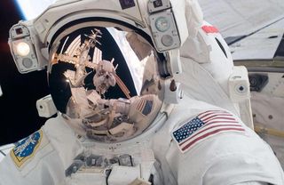 STS-124 Mission Specialist Mike Fossum participates in the mission's first spacewalk. Visible in the reflections of his helmet visor are various components of the station, Earth's horizon and astronaut Ron Garan.