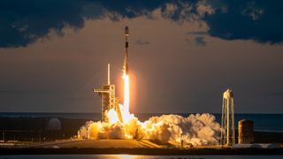 a black-and-white spacex falcon 9 rocket launches into darkening evening sky.