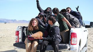 seven people hold a small rocket in the back of a white pickup truck in the desert