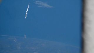 a white plume rises into the sky above the ocean from a seaside pad, as seen from the international space station