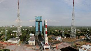 a red and white rocket rolls out to the launch pad, seen from afar in a drone image