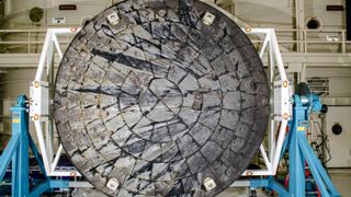 closeup of a circular gray spacecraft heat shield inside a processing building