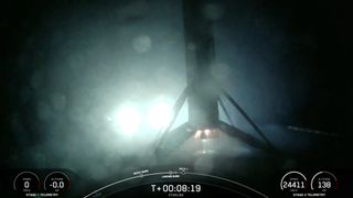 A black and white spacex falcon 9 rocket first stage sits on the deck of a ship at sea at night.