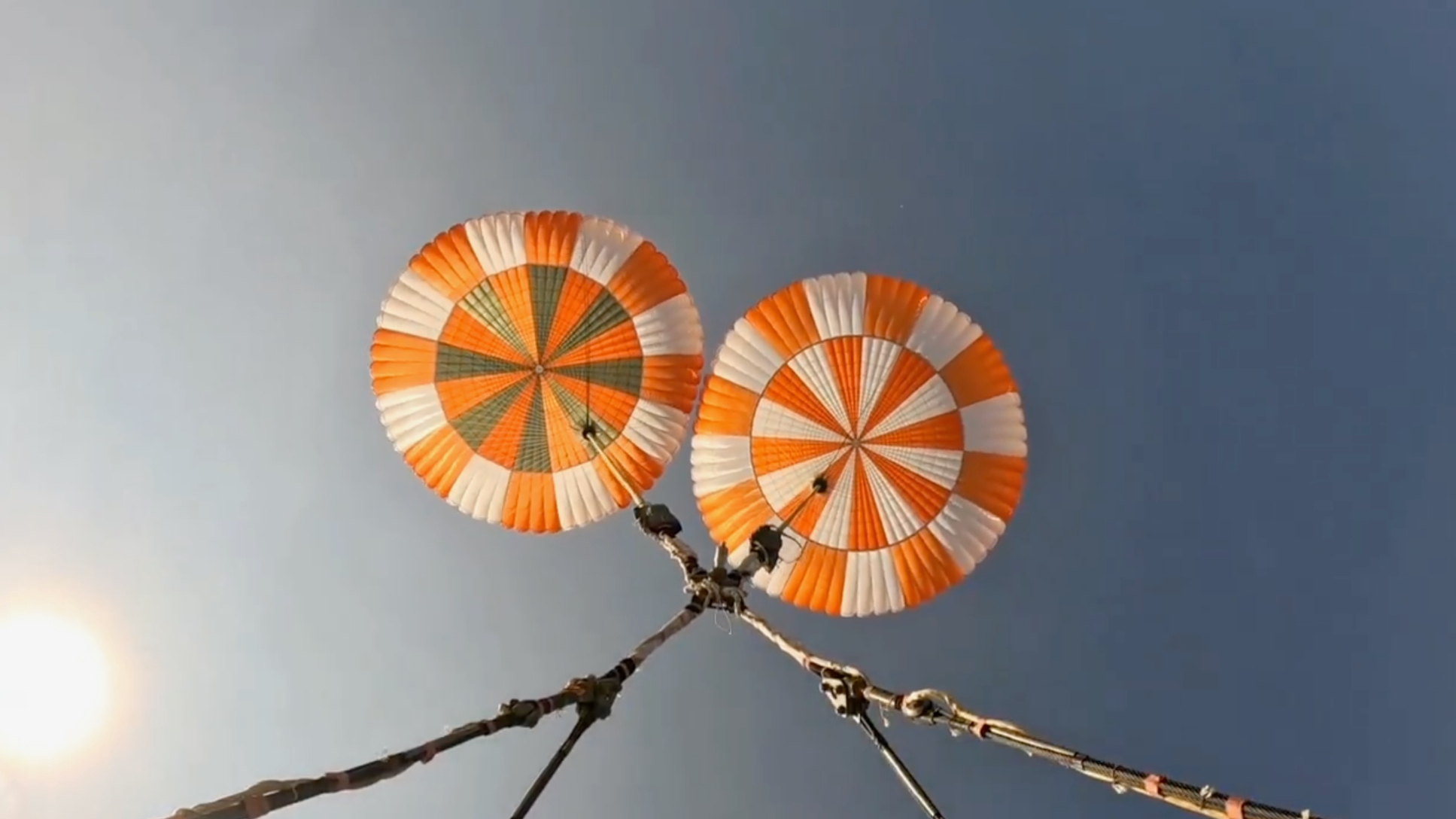 view looking up at two orange and white parachutes and a blue sky