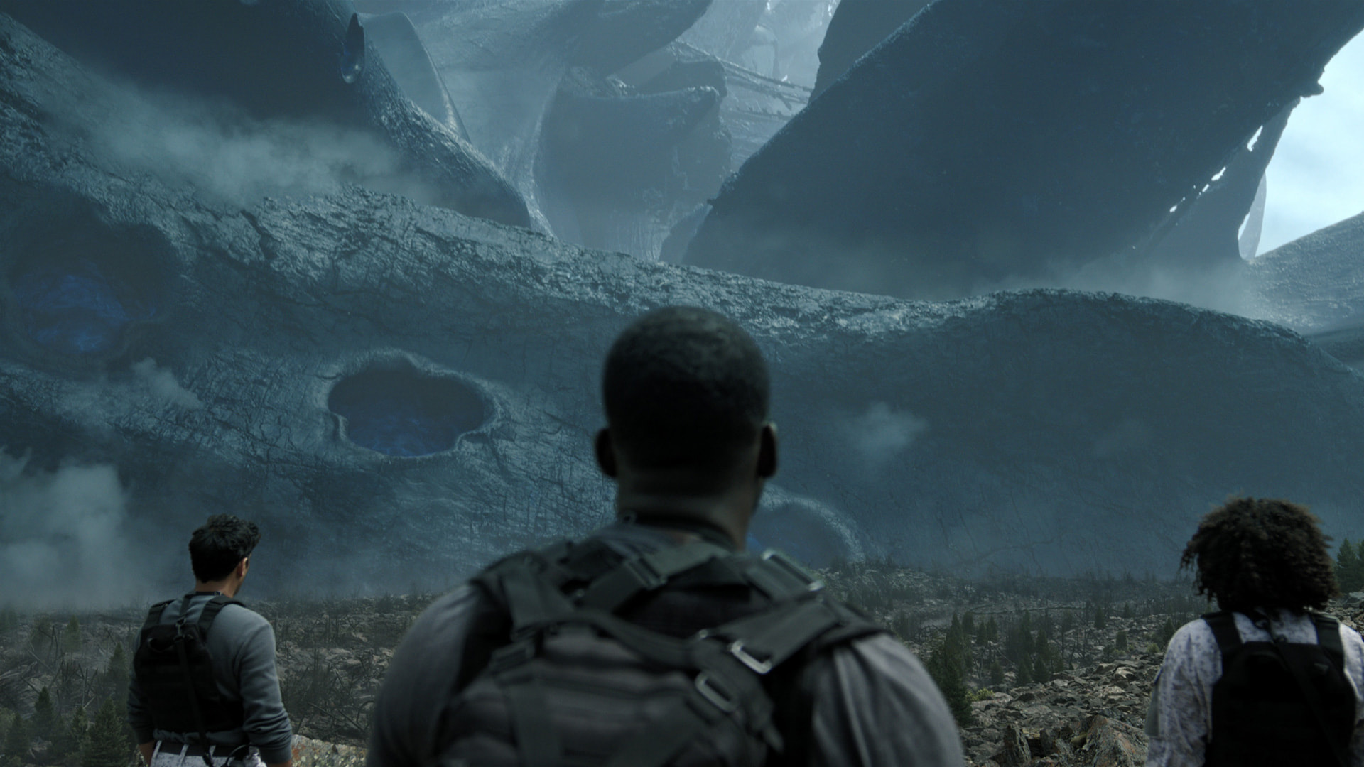 Three figures approach a massive crashed alien spaceship