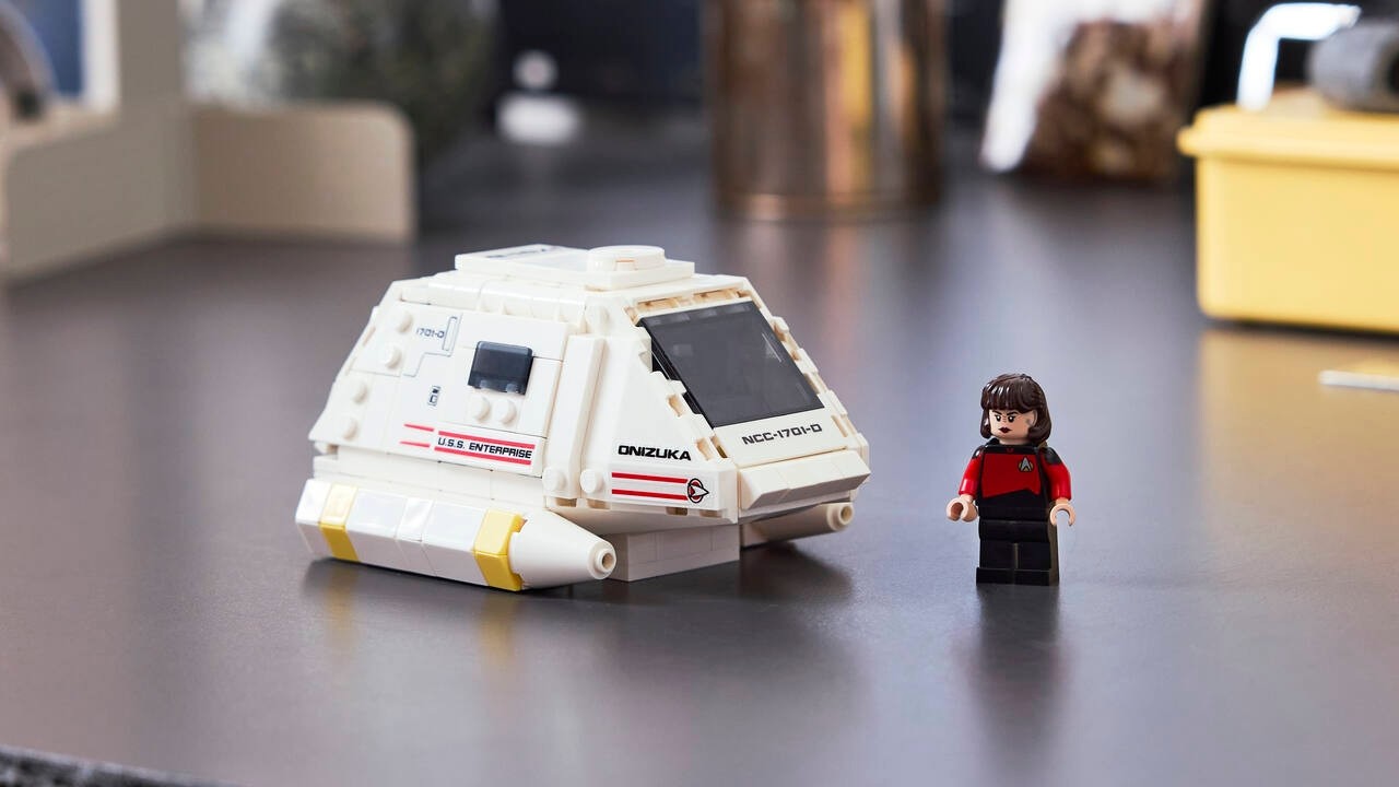 a white cube-shaped spaceship and a plastic figurine of a person in a red flight suit