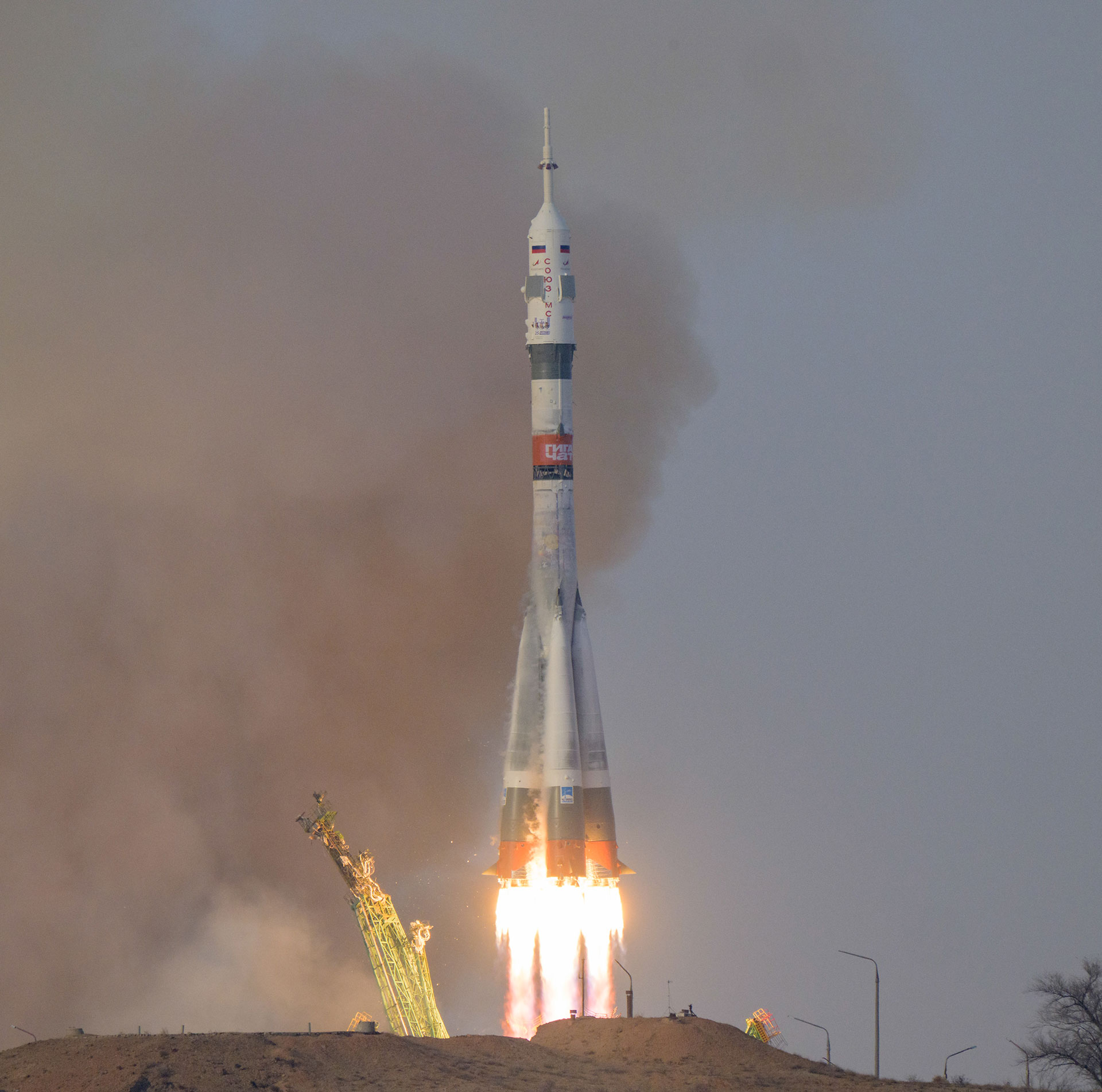 a white, olive green and orange rocket is seen lifting off on a mid-afternoon launch.