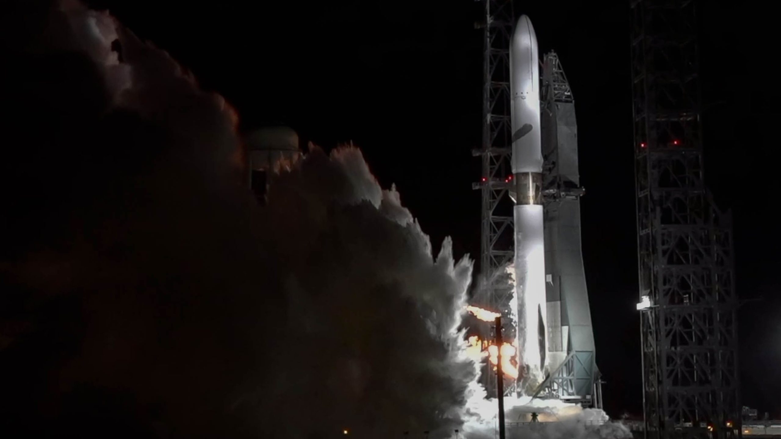 A tall white rocket spits smoke from below as its engines fire.