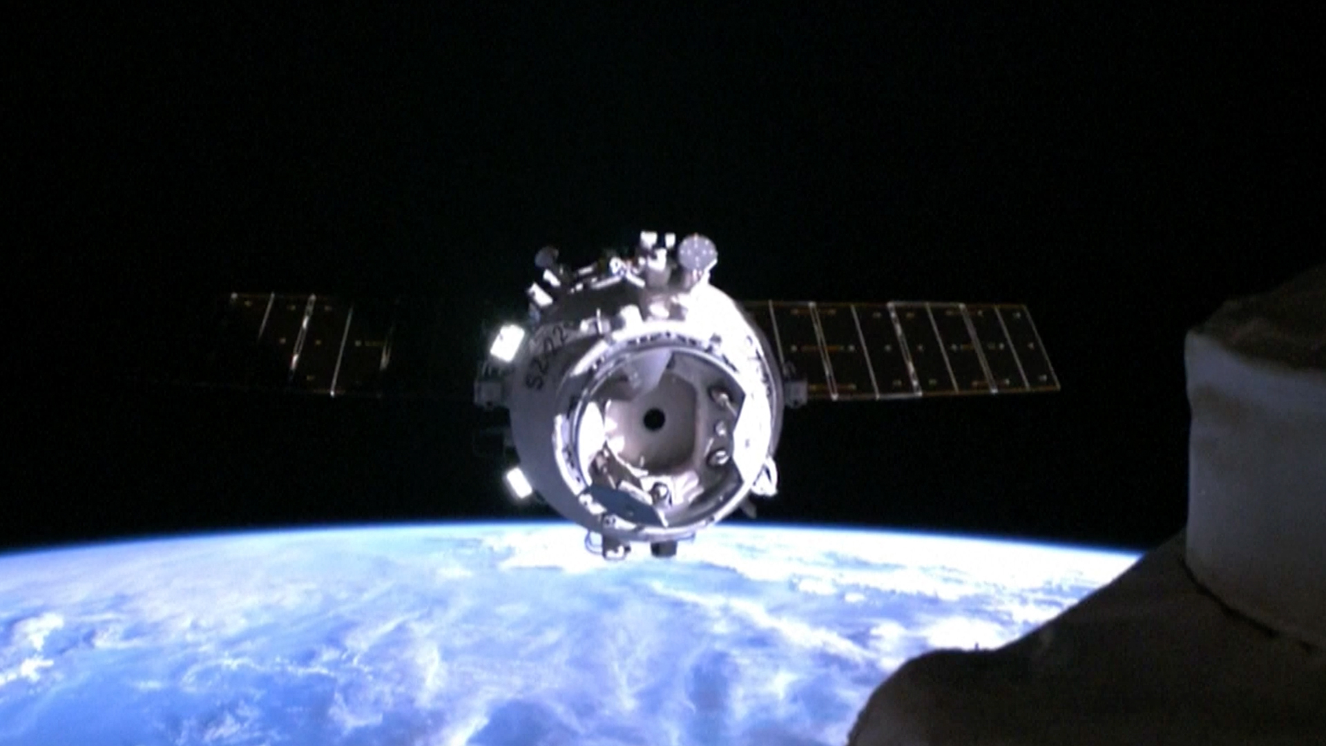 a white space capsule approaches a space station with earth in the background