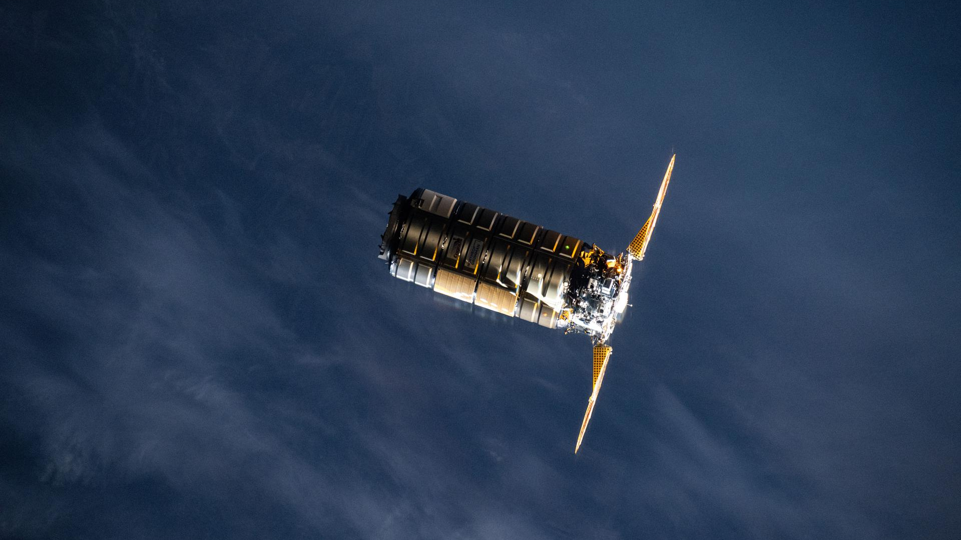 A metal spacecraft with two solar panels on either side is seen in low-Earth orbit