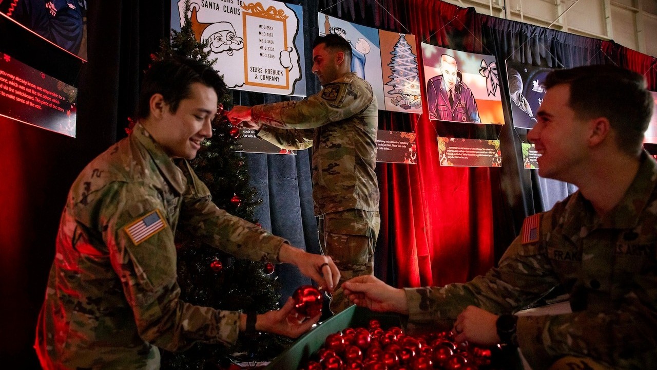 three people in military fatigues hang christmas decorations in a hangar