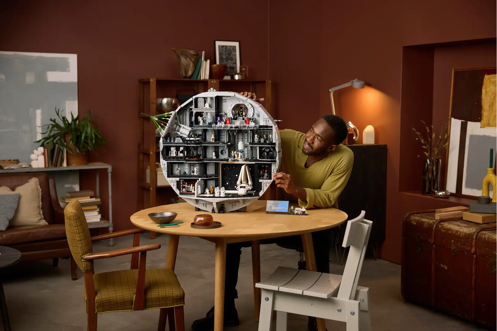 a man sitting at a table admiring a Lego Death Star