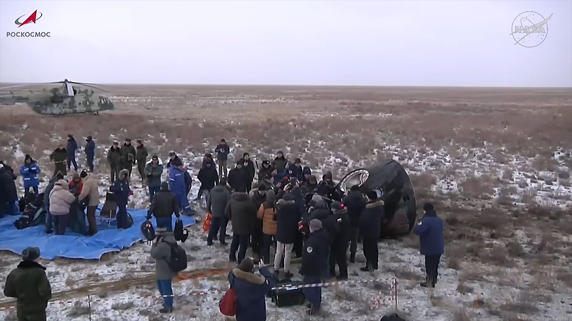 a crowd gathers around a recently landed space capsule on a snow-dusted desert landscape