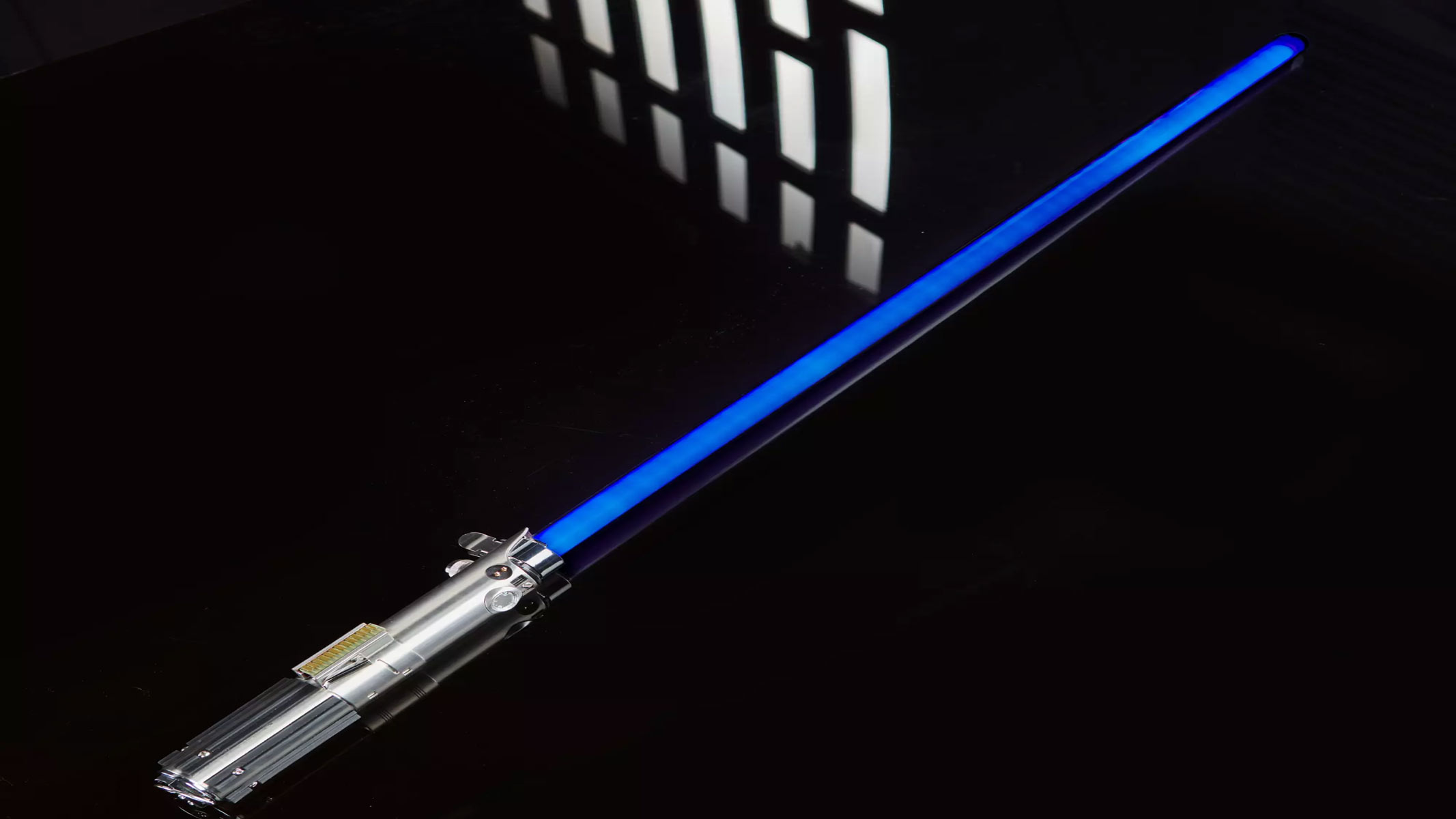 A silver metal hilt is on display as a blue lightsaber is on a black background.