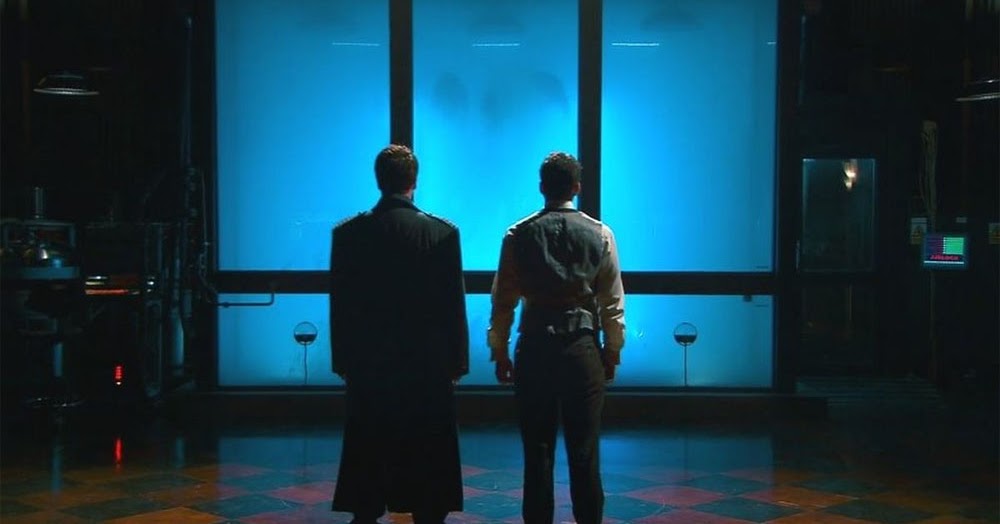 Screenshot from the 2009 mini-series Torchwood: Children of Earth showing Ianto Jones and Captain Jack Harkness looking at an alien creature in a tank of water.