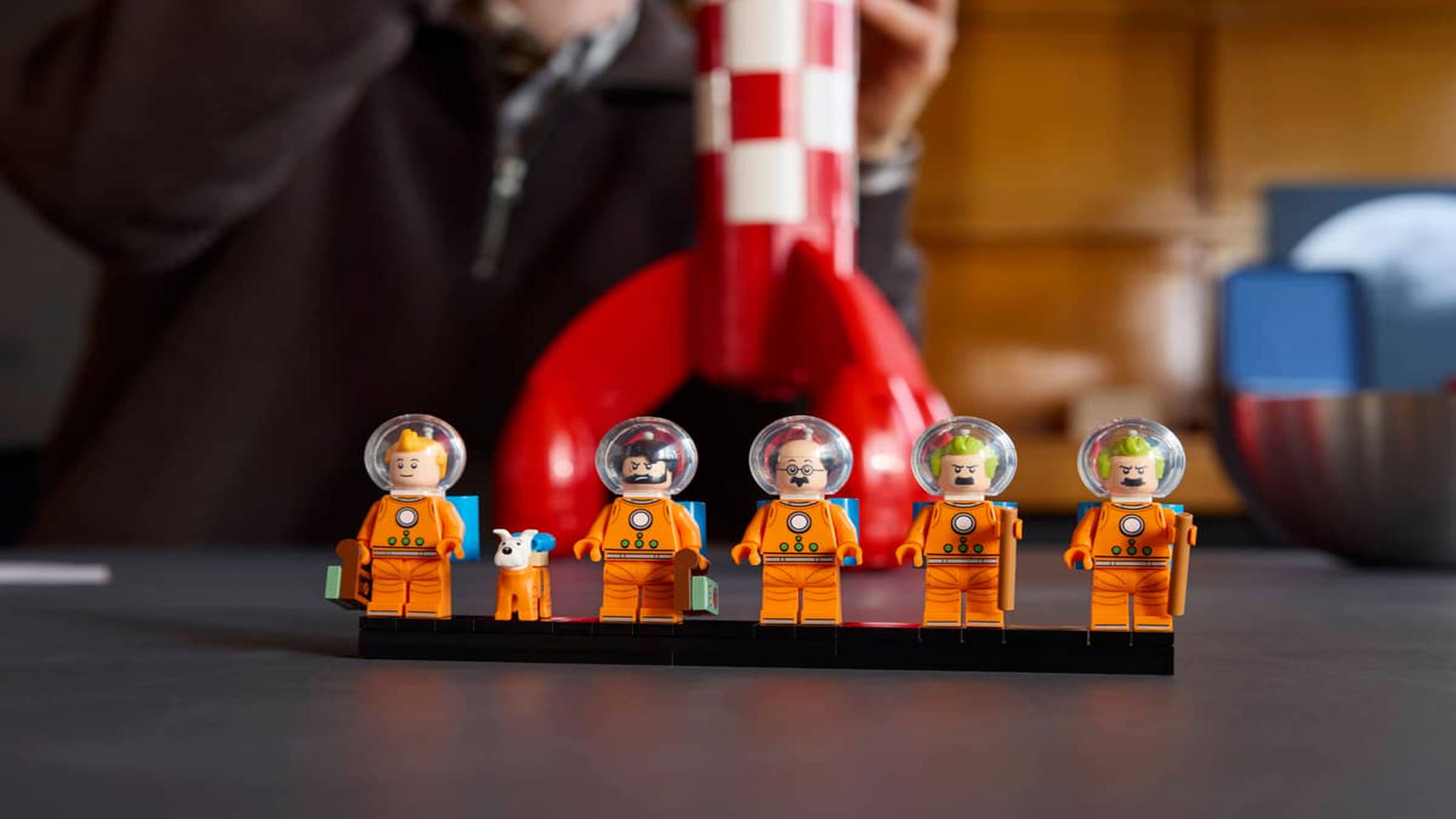 A brick built rocket featuring red and white squares on its exterior is posed alongside six astronaut figures that come with the set.