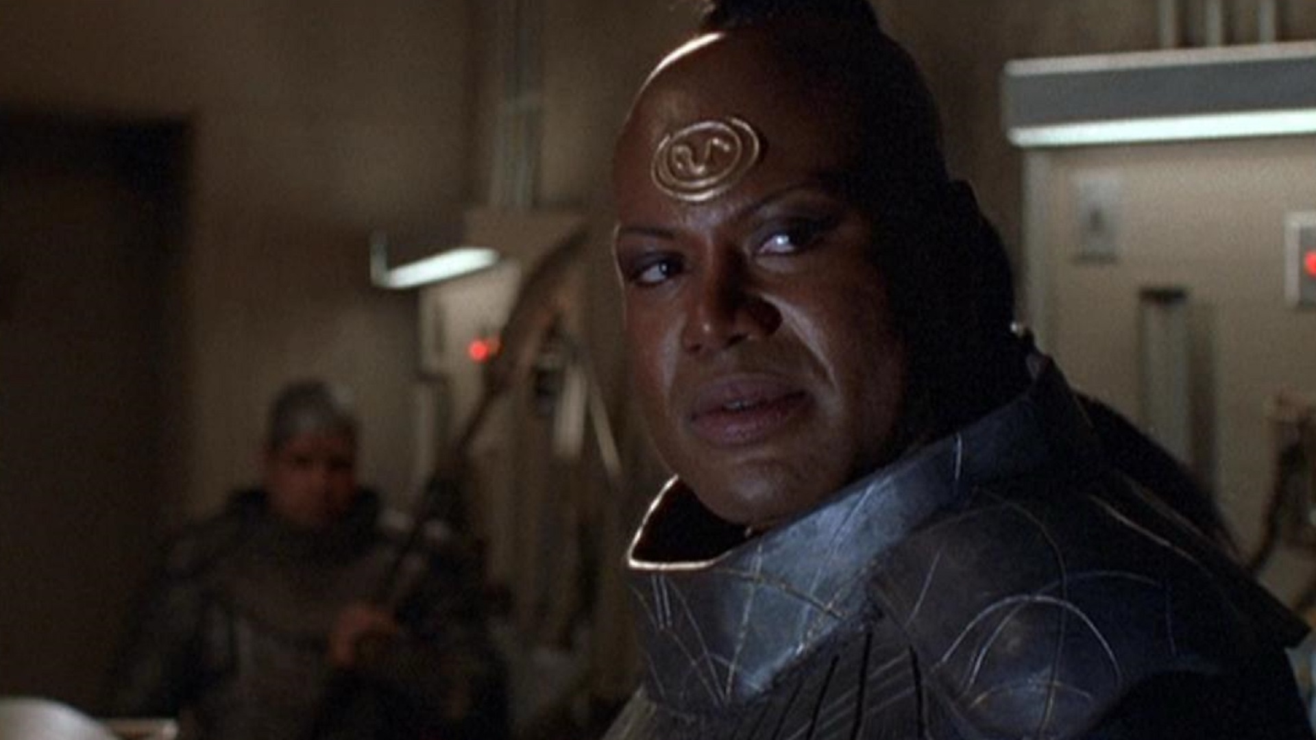 Screenshot from Stargate SG-1 showing an alien warrior with a gold symbol on his head.