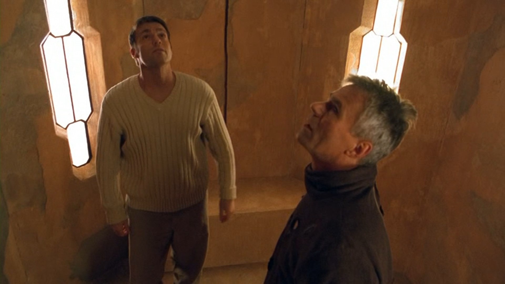 Screenshot from Stargate SG-1 showing two men looking up in a small sandstone room.